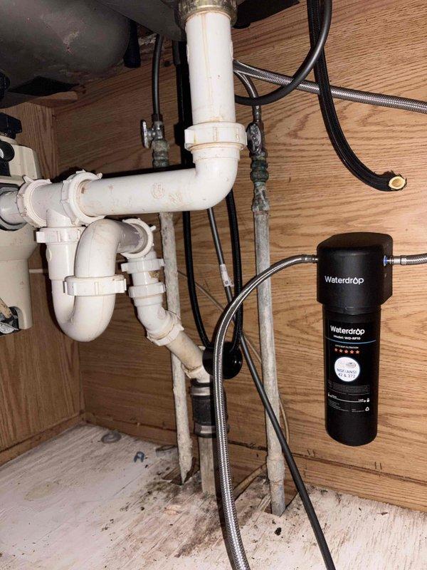 Responded to multiple plumbing issues in 90-year-old residence including slow-draining kitchen sink and lack of hot water at fixture. Inspected under-sink plumbing and identified drainage concerns with existing PVC P-trap configuration. Removed and evaluated kitchen faucet assembly to address hot water delivery issue, documenting condition of stainless steel double-basin sink, supply lines, and water filtration system. Photographed plumbing components, including Waterdrop filtration unit, braided supply lines, and drainage assembly for assessment and recommendations.