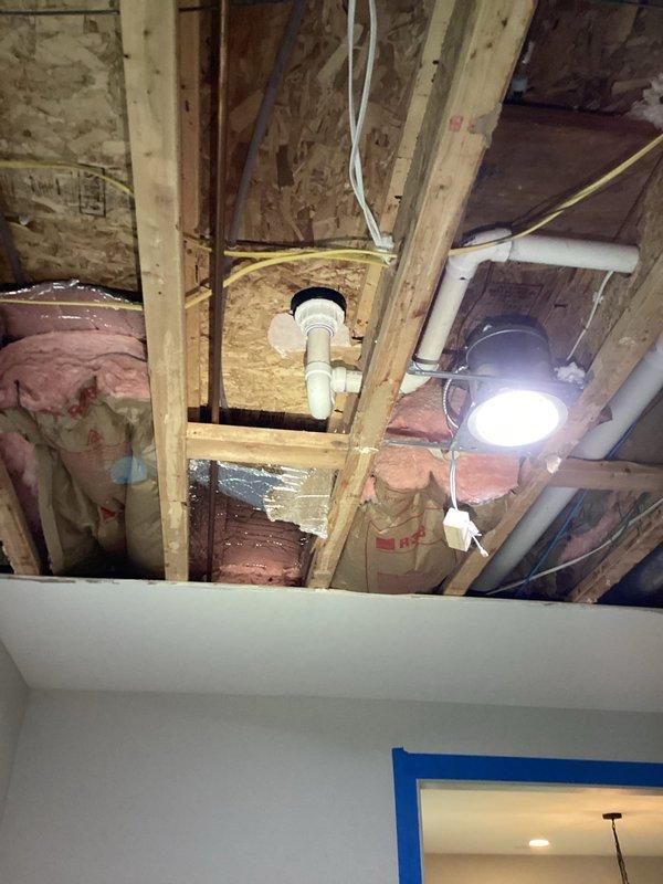 Completed reinstallation of soaking tub drain assembly in bathroom with attic access above. Accessed drain connection through ceiling space, secured white PVC drain fitting to structural framing with proper support, and verified watertight seal at tub connection. All work completed without observable leaks, with finished bathroom surfaces and herringbone tile flooring protected throughout the repair process.