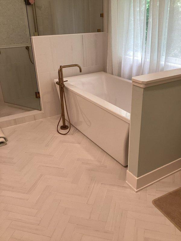 Completed reinstallation of soaking tub drain assembly in bathroom with attic access above. Accessed drain connection through ceiling space, secured white PVC drain fitting to structural framing with proper support, and verified watertight seal at tub connection. All work completed without observable leaks, with finished bathroom surfaces and herringbone tile flooring protected throughout the repair process.