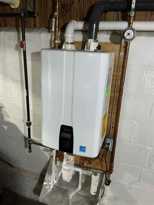 Responded to no-heat call on 2-year-old Navien tankless water heater. Upon arrival, unit was non-operational. Performed descaling flush procedure using cleaning solution and pump setup to remove mineral buildup from heat exchanger. Flushed both hot and cold side isolation valves with cleaning solution circulated through system. Verified proper operation of pre-filtration system. Unit restored to full functionality with adequate hot water production and normal operational parameters confirmed on digital display.