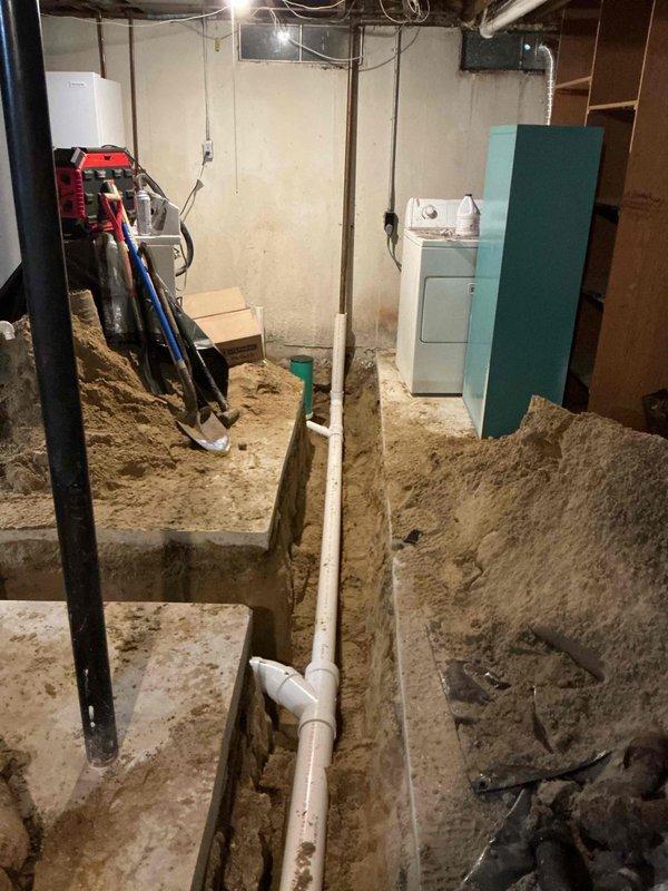 Completed comprehensive sewer lateral replacement including both internal and external components over a three-day period. Excavated basement floor by cutting and removing concrete to expose existing sewer lines, installed new white PVC drainage piping system with proper vertical and horizontal runs, and backfilled trenches with appropriate bedding material. Work performed in occupied residence with existing water heater and laundry equipment remaining in place throughout the duration of the project.