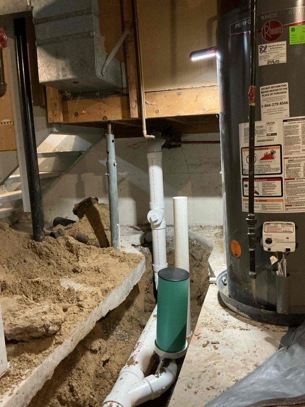 Completed comprehensive sewer lateral replacement including both internal and external components over a three-day period. Excavated basement floor by cutting and removing concrete to expose existing sewer lines, installed new white PVC drainage piping system with proper vertical and horizontal runs, and backfilled trenches with appropriate bedding material. Work performed in occupied residence with existing water heater and laundry equipment remaining in place throughout the duration of the project.