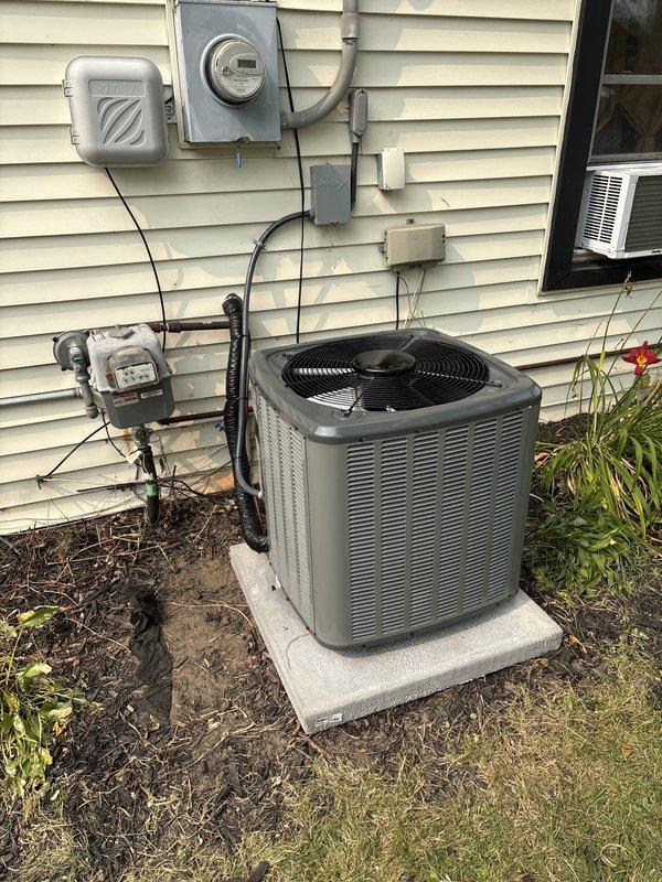 Completed full air conditioning system replacement at residential property. Removed existing outdoor condenser unit and installed new gray AC condenser on concrete pad with proper electrical connections including new disconnect switch and conduit routing to existing meter panel. Indoor installation included integration with existing furnace system, installation of new evaporator coil assembly, and proper refrigerant line connections using black flexible refrigerant lines. Verified all electrical connections meet code requirements with proper wire gauge and secure mounting of junction boxes on exterior wall. Completed condensate drainage system using white PVC piping with appropriate pitch and secured all ductwork with proper hangers and supports. Pressure tested refrigerant lines, evacuated system to proper vacuum levels, and charged unit to manufacturer specifications. Performed full system startup, verified proper airflow across evaporator coil, confirmed correct superheat and subcoo