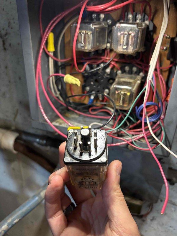 Responded to boiler issue where hot water was cross-contaminating the cold water supply following recent work by another contractor, causing the unit to run continuously. Upon inspection, identified improper wiring in the control panel affecting pump operation. Following remote technical guidance, accessed the four-inch square electrical box, opened the flat plate cover, and corrected the pump wiring by disconnecting the existing black wire and replacing it with a red wire connection using a wire nut to establish proper two-wire pump configuration. Replaced worn relay component showing significant discoloration and age-related deterioration. Documented existing control panel condition showing multiple relays, transformers, and interconnected wiring with various colored conductors. Corrected wiring resolved the cross-contamination issue and restored normal boiler cycling operation.