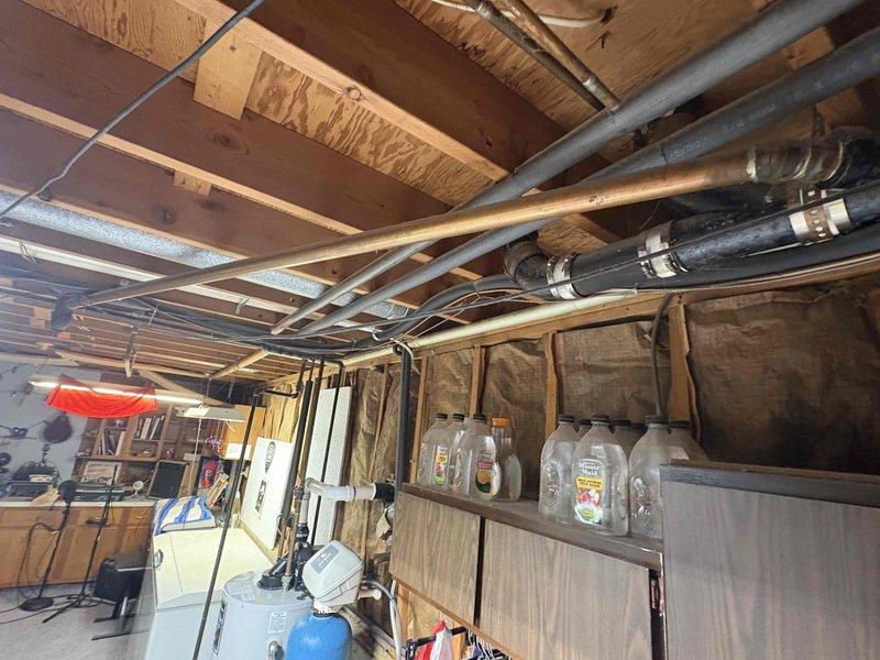Responded to complaint of gurgling tub drain when toilet flushed and strong acidic odor in 60-year-old home with septic system. Accessed plumbing system through basement/crawlspace to inspect drain and vent piping. Upon investigation, identified venting issue in drain-waste-vent system causing negative pressure when toilet discharged, resulting in gurgling at tub drain and allowing sewer gases to escape into living space. Documented existing plumbing configuration with photos showing copper drain lines, vent pipes, and connection points between fixtures to assess proper venting and drainage flow for this single-bathroom home on septic system.