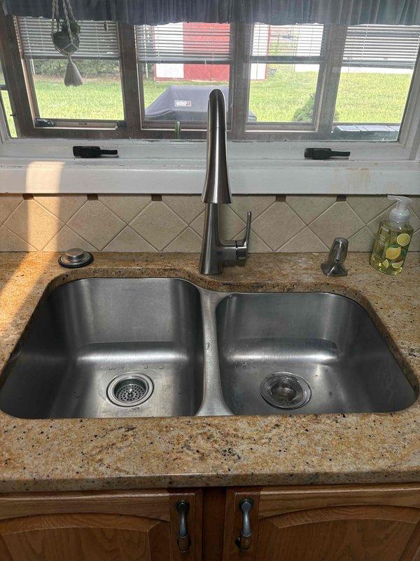 Completed kitchen faucet installation, replacing the existing fixture with a new chrome single-handle model with pull-out spray attachment. Addressed gas line concern by removing saddle clamp from 3-foot section of gas piping in the ceiling cavity, ensuring proper gas line integrity and code compliance. Verified all plumbing connections for leaks, tested faucet operation and water flow in both basins, and confirmed proper drainage function.