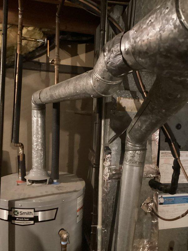 Responded to callback for ongoing no hot water issue on 8-year-old A.O. Smith water heater. Upon arrival, inspected unit and surrounding plumbing connections in basement utility area. Observed extensive condensation and moisture accumulation on HVAC ductwork and insulated piping throughout mechanical space, indicating potential humidity concerns. Photographed water heater installation, copper supply lines, and overall mechanical room conditions. Documented heavy water droplet formation on gray insulated ductwork with visible moisture saturation on vertical runs and elbow connections. Assessed plumbing configuration including copper and black iron pipe routing. Evaluated water heater operation, connections to supply lines, and integration with existing HVAC system components. Investigated root cause of recurring hot water failure and determined appropriate corrective action based on field observations and equipment age.