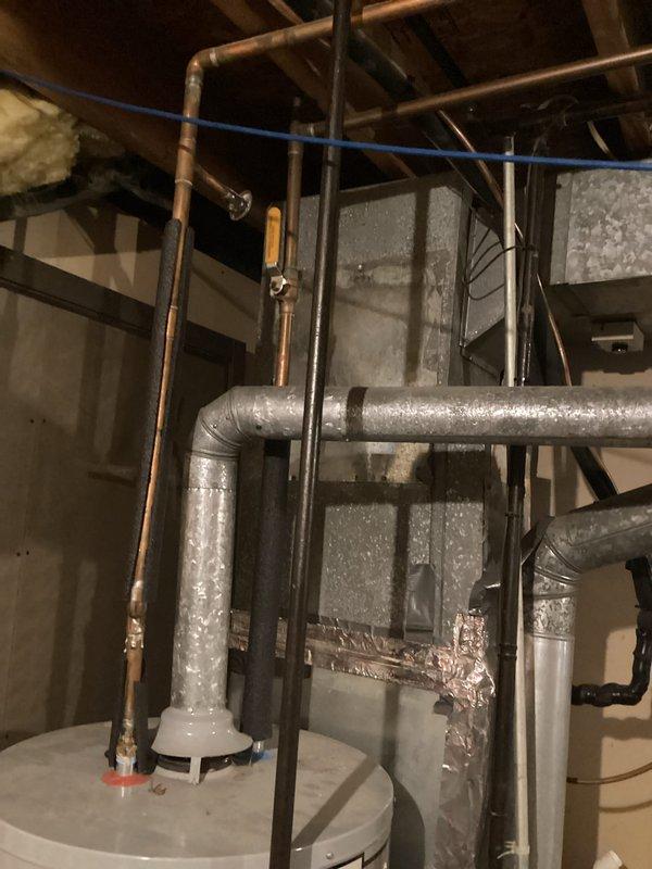 Responded to callback for ongoing no hot water issue on 8-year-old A.O. Smith water heater. Upon arrival, inspected unit and surrounding plumbing connections in basement utility area. Observed extensive condensation and moisture accumulation on HVAC ductwork and insulated piping throughout mechanical space, indicating potential humidity concerns. Photographed water heater installation, copper supply lines, and overall mechanical room conditions. Documented heavy water droplet formation on gray insulated ductwork with visible moisture saturation on vertical runs and elbow connections. Assessed plumbing configuration including copper and black iron pipe routing. Evaluated water heater operation, connections to supply lines, and integration with existing HVAC system components. Investigated root cause of recurring hot water failure and determined appropriate corrective action based on field observations and equipment age.