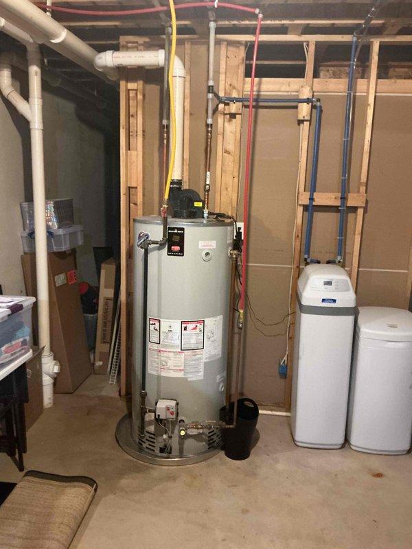 Responded to water heater leak in basement mechanical room. Upon inspection, found 10-year-old residential water heater with active leak that had been ongoing for approximately one week. Documented existing installation showing water heater with connected PEX supply lines, gas line, circulation pump, and adjacent water treatment systems. Photographed equipment and plumbing configuration for service records. Advised customer on condition and repair options for aging unit.