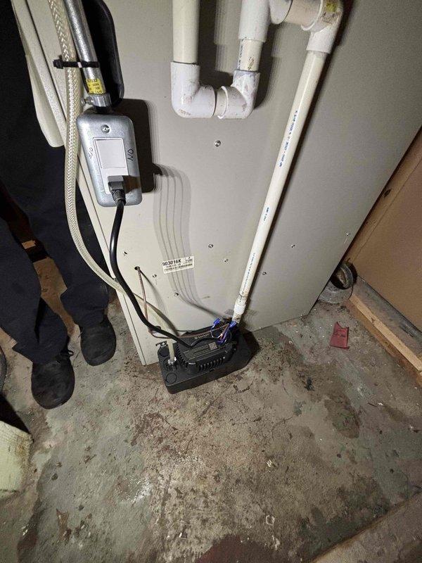 Responded to water leak complaint occurring during AC operation. Upon inspection, found condensate drain system associated with HVAC unit in utility room. Examined furnace and surrounding plumbing connections for source of moisture accumulation on concrete floor. Photographed equipment layout including water heater, furnace unit, PVC drain lines, and floor conditions showing water staining. Identified condensate drainage issue related to air conditioning cooling cycle. Documented existing water damage patterns on concrete flooring and verified all utility connections to appliances. Recommended proper condensate line maintenance and drainage system evaluation to prevent future leaking during cooling operations.