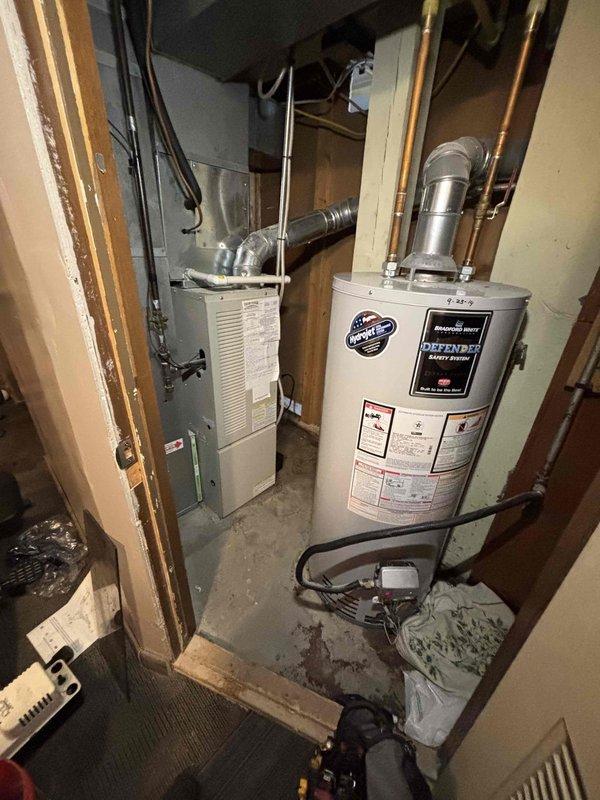 Responded to water leak complaint occurring during AC operation. Upon inspection, found condensate drain system associated with HVAC unit in utility room. Examined furnace and surrounding plumbing connections for source of moisture accumulation on concrete floor. Photographed equipment layout including water heater, furnace unit, PVC drain lines, and floor conditions showing water staining. Identified condensate drainage issue related to air conditioning cooling cycle. Documented existing water damage patterns on concrete flooring and verified all utility connections to appliances. Recommended proper condensate line maintenance and drainage system evaluation to prevent future leaking during cooling operations.