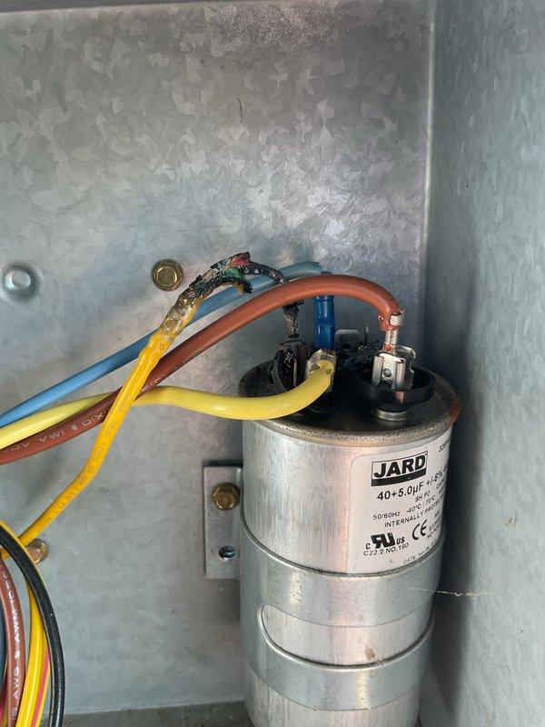 Responded to no cooling call and found outdoor unit running but no airflow from interior vents. Upon inspection, discovered failed dual-run capacitor with visible burn damage and deterioration at terminal connections. Replaced defective JARD 40+5.0µF capacitor with new unit, restored all electrical connections, and verified system operation. Unit now cooling properly with normal airflow restored to all vents.