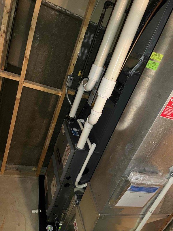 Completed full HVAC system installation including new furnace and air conditioning condenser unit. Installed outdoor AC condenser on gravel pad against building exterior with proper refrigerant line connections and electrical hookup. Inside mechanical room, installed new furnace with complete PVC venting system secured to wall framing, connected condensate drainage lines, and integrated ductwork to existing distribution system. All equipment tested and verified operational upon completion.