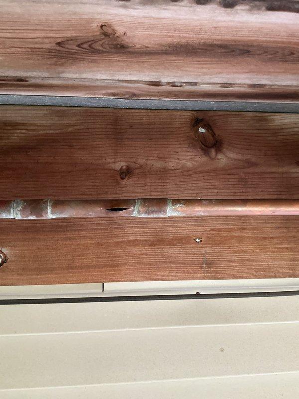 Responded to plumbing leak emergency involving a burst pipe located underneath the deck structure. Upon arrival, confirmed the outside water supply had been previously shut off by the homeowner. Conducted inspection of the affected area beneath the deck, documenting the burst pipe location and assessing the extent of water damage to surrounding wooden deck framing and structural components. Additionally inspected and addressed a separate water leak identified under the kitchen sink. Captured photographic documentation of the deck underside showing wooden construction materials, framing elements, and structural assembly where the burst pipe was located.