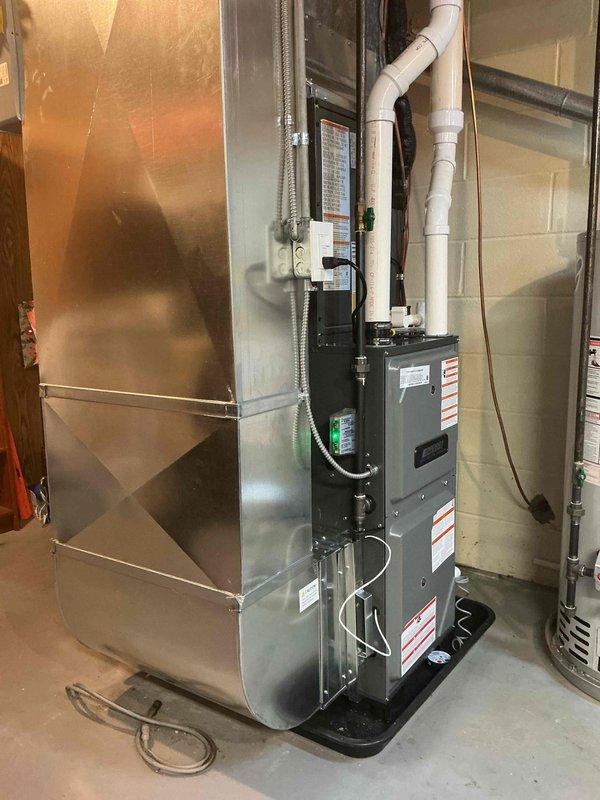 Completed full HVAC system installation including new furnace and air conditioning unit at residential property. Installed gray furnace with proper drain pan in mechanical room, connected to metallic air handler with integrated ductwork system. Mounted exterior AC condenser unit on concrete pad with appropriate electrical disconnect, conduit runs, and PVC drainage piping. All equipment properly positioned, vented, and connected per manufacturer specifications and local code requirements.