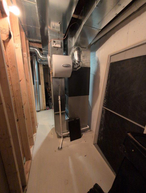 Completed full air conditioning system replacement in basement mechanical room. Installed new HVAC unit with metallic gray furnace featuring integrated cooling system, mounted to wall with proper elevation and support stands. Connected all supply and return ductwork using galvanized metal ducts and flexible ducting, routing through ceiling area to existing distribution system. Installed electrical connections and control panel, verified all refrigerant lines and condensate drainage properly secured. Tested system operation for proper airflow, temperature differential, and thermostat communication. All equipment installed per manufacturer specifications and local code requirements.