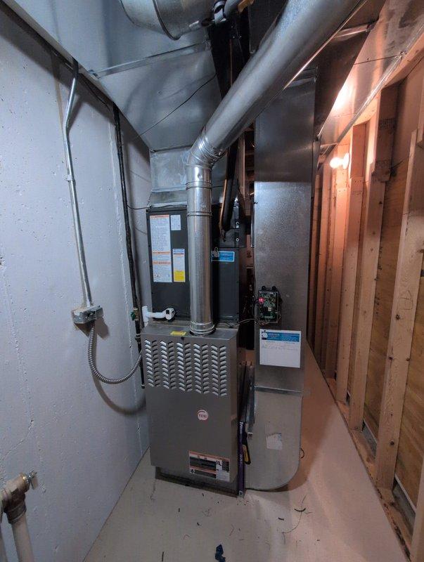 Completed full air conditioning system replacement in basement mechanical room. Installed new HVAC unit with metallic gray furnace featuring integrated cooling system, mounted to wall with proper elevation and support stands. Connected all supply and return ductwork using galvanized metal ducts and flexible ducting, routing through ceiling area to existing distribution system. Installed electrical connections and control panel, verified all refrigerant lines and condensate drainage properly secured. Tested system operation for proper airflow, temperature differential, and thermostat communication. All equipment installed per manufacturer specifications and local code requirements.