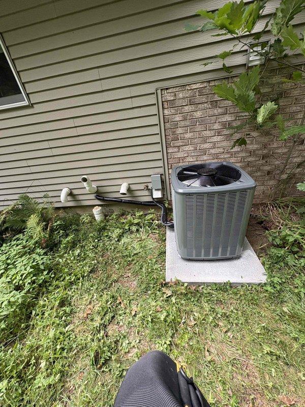 Complete residential HVAC system replacement performed, including outdoor condensing unit and indoor air handler components. Removed existing equipment and installed new AirEase brand furnace and air handler in basement utility area. Outdoor gray condensing unit with dual-fan configuration positioned on existing concrete pad against exterior wall with proper clearances maintained. Installed white PVC condensate drainage lines with appropriate slope and secured routing along foundation using mounting straps. Ran copper refrigerant lines vertically through structure connecting outdoor and indoor components. Connected system to existing ductwork and verified all metallic duct connections sealed properly. Installed electrical disconnect box at outdoor unit location per code requirements. Completed all electrical connections and verified proper voltage supply to equipment. Pressure-tested refrigerant lines for leaks, evacuated system, and charged to manufacturer specifications. Started syst