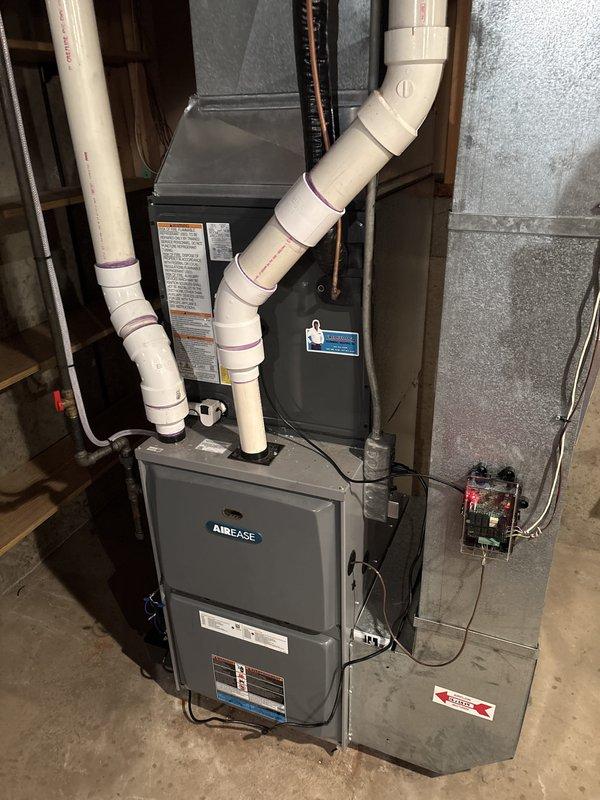 Complete residential HVAC system replacement performed, including outdoor condensing unit and indoor air handler components. Removed existing equipment and installed new AirEase brand furnace and air handler in basement utility area. Outdoor gray condensing unit with dual-fan configuration positioned on existing concrete pad against exterior wall with proper clearances maintained. Installed white PVC condensate drainage lines with appropriate slope and secured routing along foundation using mounting straps. Ran copper refrigerant lines vertically through structure connecting outdoor and indoor components. Connected system to existing ductwork and verified all metallic duct connections sealed properly. Installed electrical disconnect box at outdoor unit location per code requirements. Completed all electrical connections and verified proper voltage supply to equipment. Pressure-tested refrigerant lines for leaks, evacuated system, and charged to manufacturer specifications. Started syst