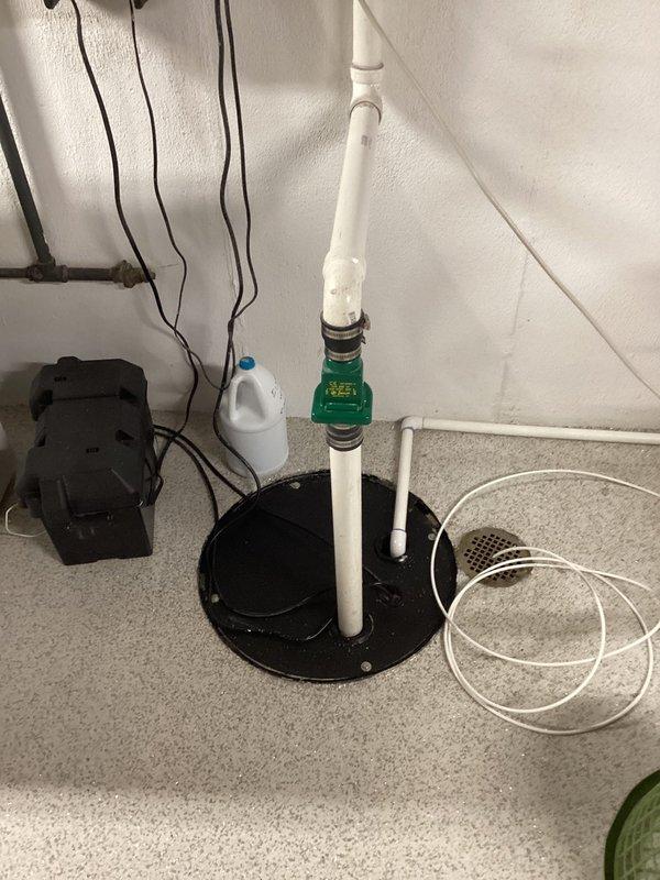 Responded to service call for sump pump backup with black sludge discharge from unit over 8 years old. Upon inspection, assessed existing sump pump system with PVC discharge piping and floor-mounted basin installation. Documented equipment condition and basement utility area configuration, noting pump age and operational failure requiring attention.