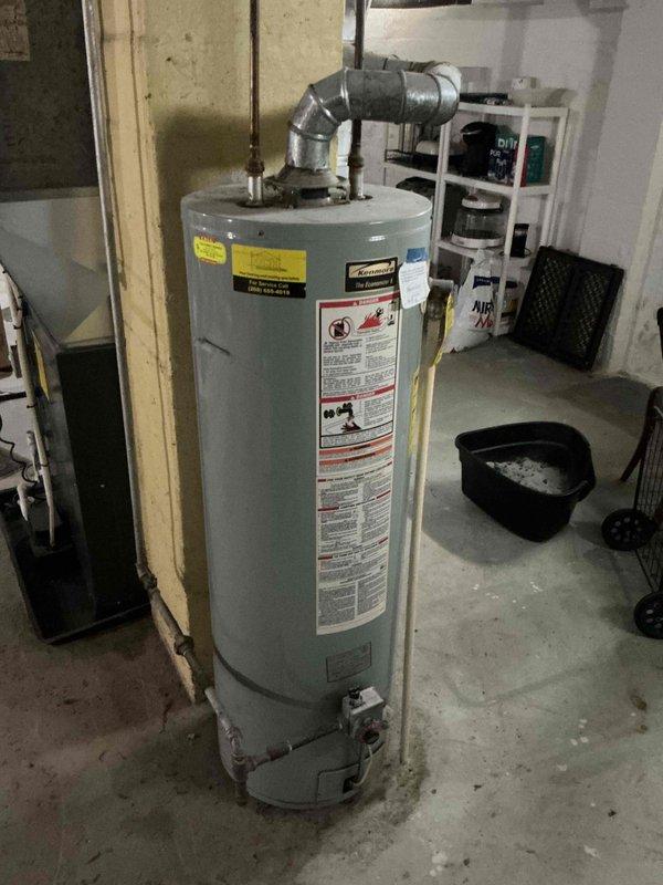 Completed estimate for residential gas-fired water heater replacement located in basement utility area. Unit assessed is a standard cylindrical tank-style water heater with visible wear, featuring top-mounted temperature and pressure relief valve, gas control assembly at base, and standard safety labeling. Documented existing installation including plumbing connections, gas line configuration, and current positioning on concrete floor for replacement specifications and material requirements.