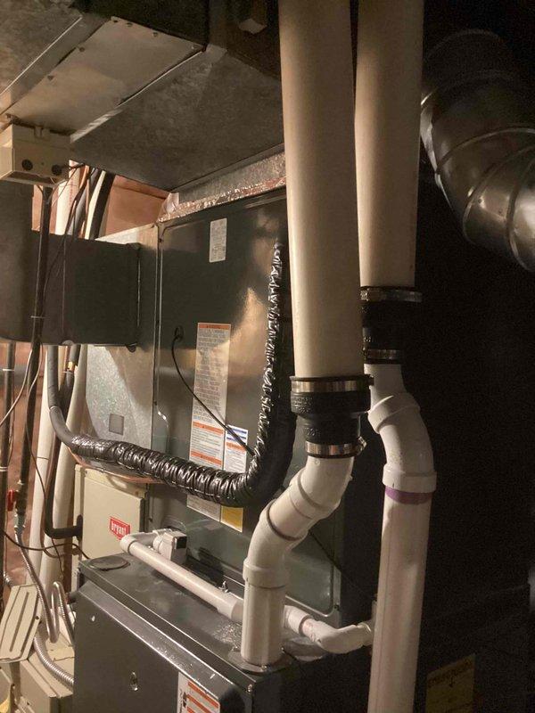 Completed full air conditioning system replacement at residential property. Removed existing aged cylindrical condenser unit and installed new Trane condensing unit in outdoor carport area against exterior wall. Replaced indoor air handler unit in basement mechanical room with new equipment. Installed new refrigerant line set with proper insulation, ran electrical conduit and wiring to both indoor and outdoor components, and connected PVC condensate drainage lines with appropriate fittings and supports. Verified all connections, tested system operation, and confirmed proper airflow through existing ductwork.
