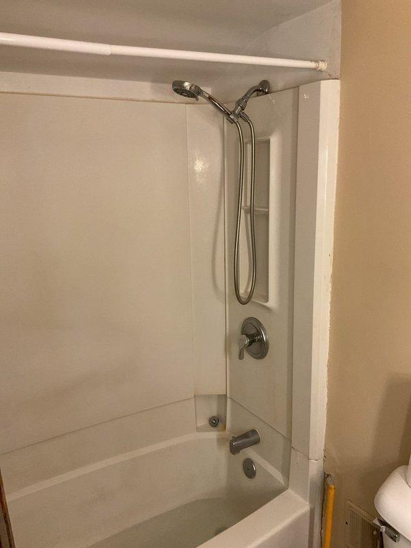 Conducted on-site assessment of leaking plumbing in upstairs bathroom of 70-year-old residential property. Inspected bathtub and shower combination unit, identifying compromised pipe requiring removal and replacement. Documented existing conditions including white tile surround, chrome fixtures, and current plumbing configuration with photographs for estimate preparation prior to commencing repair work.