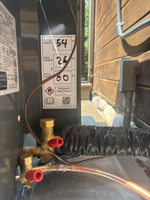 Successfully completed full air conditioning system replacement at residential property. Removed existing outdoor condensing unit and installed new high-efficiency AC condenser on wooden deck adjacent to exterior wall. Unit positioned on protective rubber pad with proper clearances maintained for airflow and serviceability.

Installed new refrigerant lines with black insulation running from outdoor unit through exterior wall to indoor air handler. Mounted electrical disconnect box on exterior siding per code requirements. System charged with refrigerant per manufacturer specifications - factory charge of 54 oz plus field charge of 26 oz for total system charge of 80 oz. Refrigerant type classified as A2L safety group per updated environmental standards.

Connected and secured all copper refrigerant lines with brass service valves and protective caps installed on both suction and liquid lines. Verified all electrical connections, tested unit operation including compressor and condenser 
