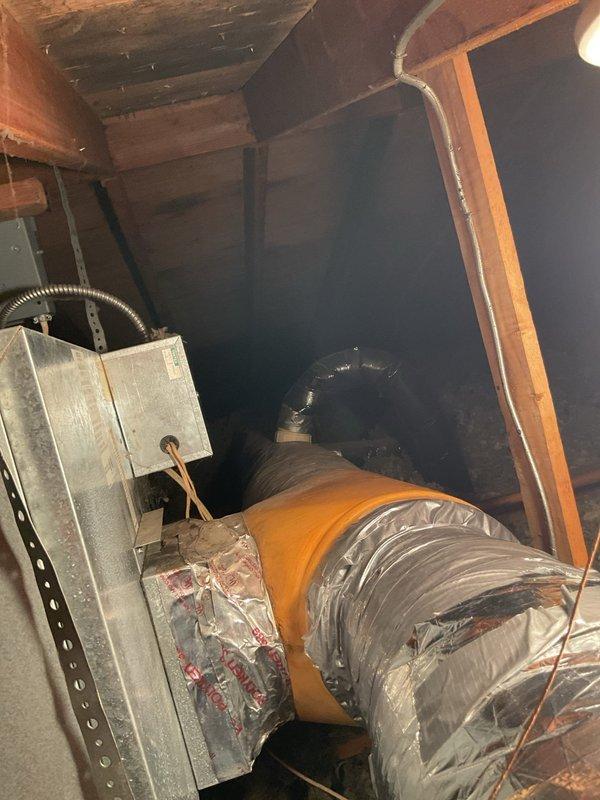 Conducted on-site evaluation for air conditioning system replacement in single-family residence. Existing HVAC unit assessed at 25 years old, well beyond typical service life expectancy. Documented current system configuration including attic-mounted equipment, flexible ductwork with insulated jacket, and metal plenum components. Photographed existing installation showing galvanized steel duct box, flexible ducting with characteristic ribbing and orange/amber outer jacket, and black condensate or refrigerant line routing through wooden attic framing. Prepared comprehensive replacement estimate based on current system layout and structural conditions observed.