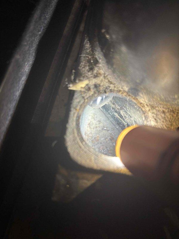 # No Cool Service Call - Clogged Drain Line and Maintenance

Responded to a no cool service call on an approximately 20-year-old air conditioning system. Upon inspection, found the unit was still providing cooling but had a clogged condensate drain line coming out of the evaporator coil. Cleared the blockage in the drain pipe to restore proper condensate flow and prevent potential water damage or secondary drain pan overflow.

Performed visual inspection of the system components, noting significant age-related deterioration throughout the unit. Observed heavy corrosion and rust buildup on the refrigerant line connections at the evaporator coil penetration points, with orange-brown oxidation deposits concentrated around the copper tubing pass-throughs in the galvanized metal housing. The outdoor unit showed extensive weathering with visible rust on the cabinet panels and framework. Insulated suction line displayed yellowing and deterioration of the insulation material consistent with th