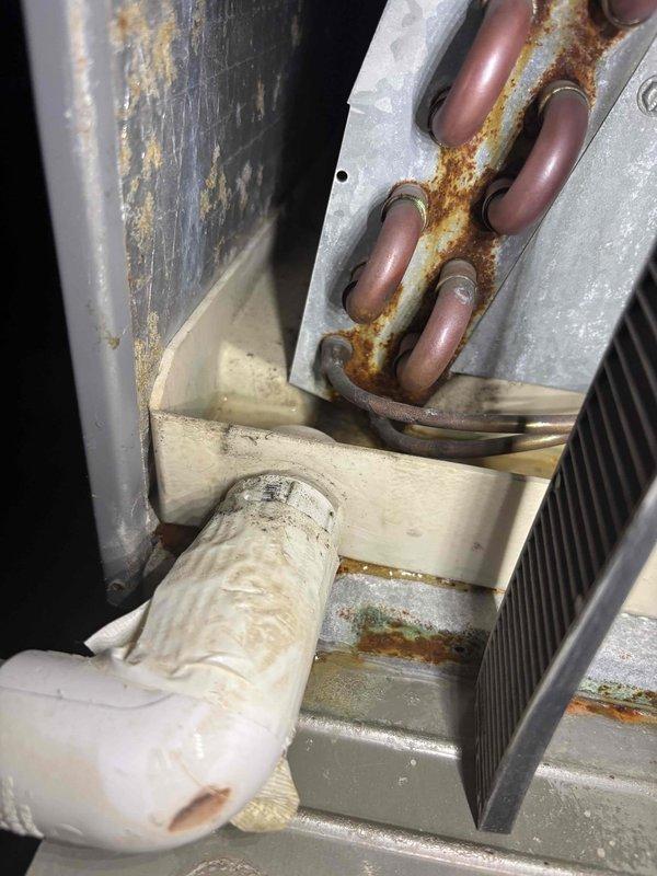 # No Cool Service Call - Clogged Drain Line and Maintenance

Responded to a no cool service call on an approximately 20-year-old air conditioning system. Upon inspection, found the unit was still providing cooling but had a clogged condensate drain line coming out of the evaporator coil. Cleared the blockage in the drain pipe to restore proper condensate flow and prevent potential water damage or secondary drain pan overflow.

Performed visual inspection of the system components, noting significant age-related deterioration throughout the unit. Observed heavy corrosion and rust buildup on the refrigerant line connections at the evaporator coil penetration points, with orange-brown oxidation deposits concentrated around the copper tubing pass-throughs in the galvanized metal housing. The outdoor unit showed extensive weathering with visible rust on the cabinet panels and framework. Insulated suction line displayed yellowing and deterioration of the insulation material consistent with th