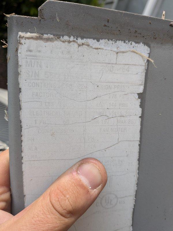 Responded to cooling complaint where air conditioning system was not reaching set temperature but maintaining partial cooling capacity. Upon arrival, inspected outdoor condensing unit and found manufacturer data plate severely deteriorated with illegible information, preventing accurate system age verification and model identification. During inspection, discovered water heater in close proximity showing active leak at base with significant rust-colored water accumulation and staining on floor, indicating potential secondary issue requiring attention. Documented equipment conditions with photos for service records.