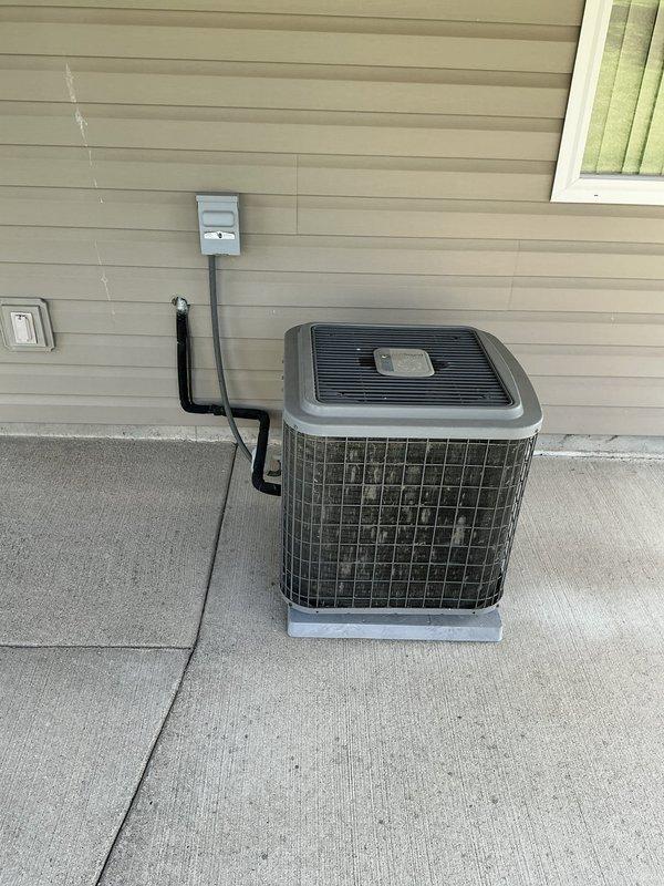 Completed estimate for furnace and air conditioning system replacement at residential property with non-operational AC unit. Documented existing outdoor condenser unit positioned on concrete pad with electrical disconnect box and conduit connections, as well as covered patio installation area with existing electrical infrastructure and thermostat controls mounted on exterior wall.