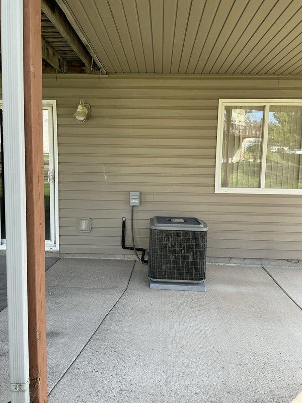 Completed estimate for furnace and air conditioning system replacement at residential property with non-operational AC unit. Documented existing outdoor condenser unit positioned on concrete pad with electrical disconnect box and conduit connections, as well as covered patio installation area with existing electrical infrastructure and thermostat controls mounted on exterior wall.