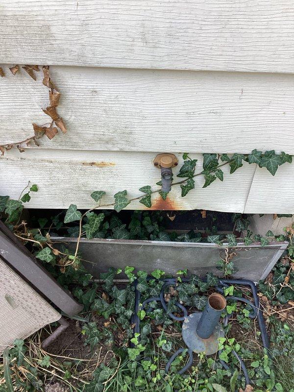 Responded to service call for low water pressure issue and frost-free faucet installation request. Upon arrival, inspected exterior plumbing connections and identified existing hose bibb penetration through building siding with vegetation growth around fixture area. Assessed current plumbing configuration including visible copper supply lines and galvanized ductwork in crawlspace or basement area beneath structure. Documented existing conditions showing weathered exterior siding, mounting hardware locations, and accessibility of plumbing penetrations for potential frost-free faucet installation points.
