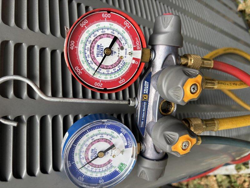 Replaced failed suction line service port on air conditioning system due to severe corrosion and oxidation of original brass fitting. Connected manifold gauges to verify system pressures and proper refrigerant charge following port replacement, confirming unit returned to normal operating parameters.