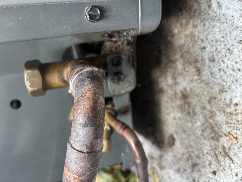 Replaced failed suction line service port on air conditioning system due to severe corrosion and oxidation of original brass fitting. Connected manifold gauges to verify system pressures and proper refrigerant charge following port replacement, confirming unit returned to normal operating parameters.