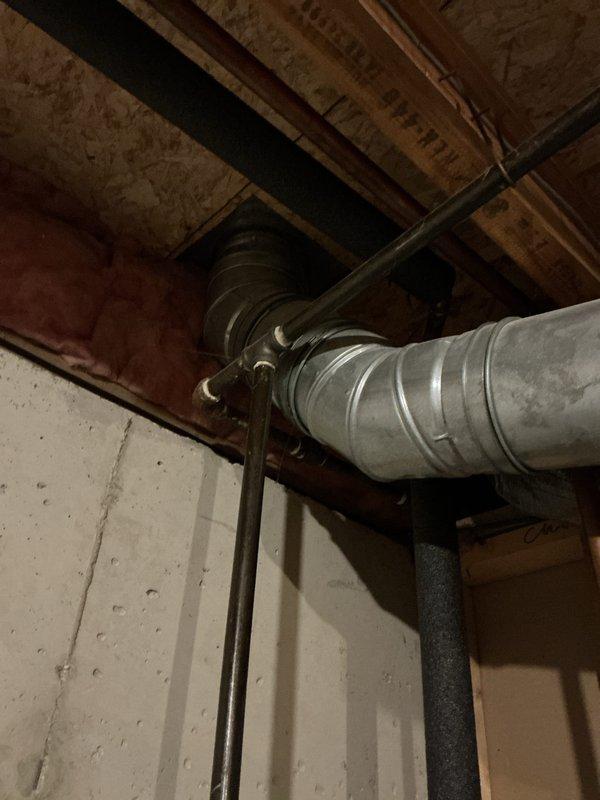 Provided estimate for water heater replacement in basement utility area. Existing white cylindrical water heater assessed with copper piping connections, pressure relief valve, and current integration with overhead HVAC ductwork system. Documented installation space including exposed wooden joists, OSB ceiling panels, galvanized metal ventilation ducts, and structural framing to determine optimal replacement configuration and ensure proper clearances for new unit installation.