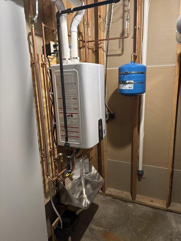 Successfully completed installation of a wall-mounted tankless water heater system in utility room with exposed framing. Installation included mounting the tankless unit to wall studs, running copper supply lines with brass shut-off valves and fittings, installing a blue expansion tank with proper suspension mounting, and connecting black PVC ventilation piping. Added condensate collection tray beneath unit for proper drainage, integrated gas line connections with safety valves, and completed all hot and cold water plumbing connections using copper piping throughout. All components were professionally mounted, properly secured to framing, and tested for operation to ensure safe and efficient performance of the complete tankless water heating system.