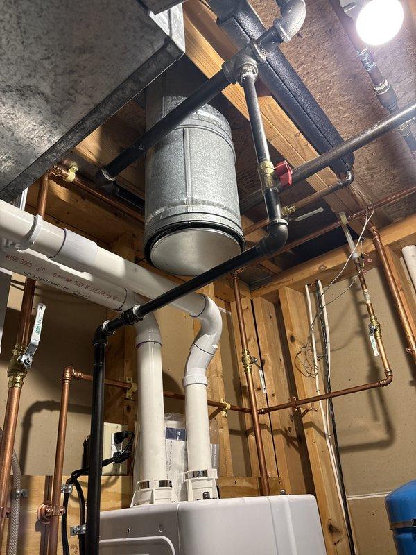 Successfully completed installation of a wall-mounted tankless water heater system in utility room with exposed framing. Installation included mounting the tankless unit to wall studs, running copper supply lines with brass shut-off valves and fittings, installing a blue expansion tank with proper suspension mounting, and connecting black PVC ventilation piping. Added condensate collection tray beneath unit for proper drainage, integrated gas line connections with safety valves, and completed all hot and cold water plumbing connections using copper piping throughout. All components were professionally mounted, properly secured to framing, and tested for operation to ensure safe and efficient performance of the complete tankless water heating system.