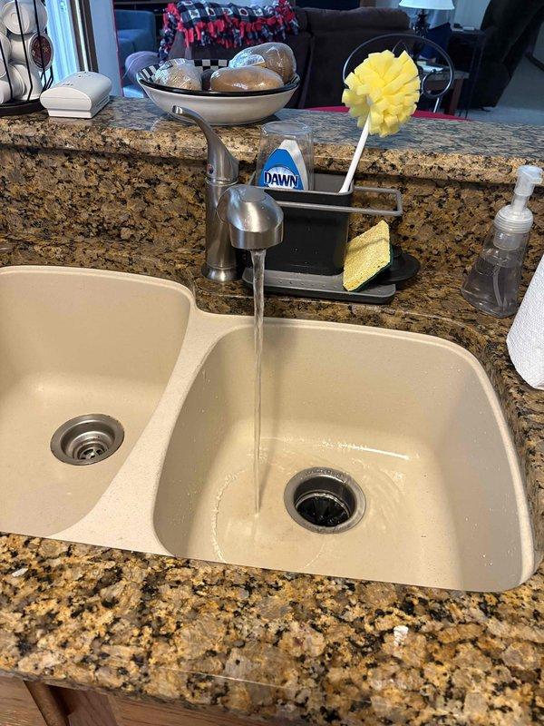 Responded to plumbing leak complaint at kitchen sink location. Upon inspection, identified active leak originating from lower section of garbage disposal unit in double-basin sink configuration. Examined disposal mounting assembly, drain connections, and associated plumbing components including white PVC P-trap system. Documented existing conditions showing black ribbed garbage disposal unit with metal mounting bracket and corrugated discharge hose connection to drain line. Assessed leak source at disposal housing and connection points to determine appropriate repair solution.