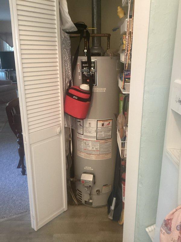 Provided estimate for tankless water heater replacement at vacation home property. Existing unit is an 8-year-old Bradford conventional tank-style water heater located in interior utility closet with louvered bifold door access. Current installation includes circulation pump mounted on top of unit, copper and plastic supply lines, and metal vent pipe extending through ceiling. Documented existing equipment configuration, closet dimensions, and venting arrangement to prepare comprehensive proposal for tankless conversion including necessary gas line, venting, and plumbing modifications required for installation.