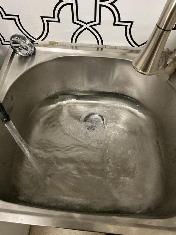 Replaced existing laundry tub with new stainless steel utility sink mounted on white cabinet base with brushed nickel hardware. Installed modern pull-down faucet with brushed nickel finish and connected supply lines. Installed standpipe assembly for washing machine discharge with proper drainage connections and secured all plumbing fixtures to code specifications.