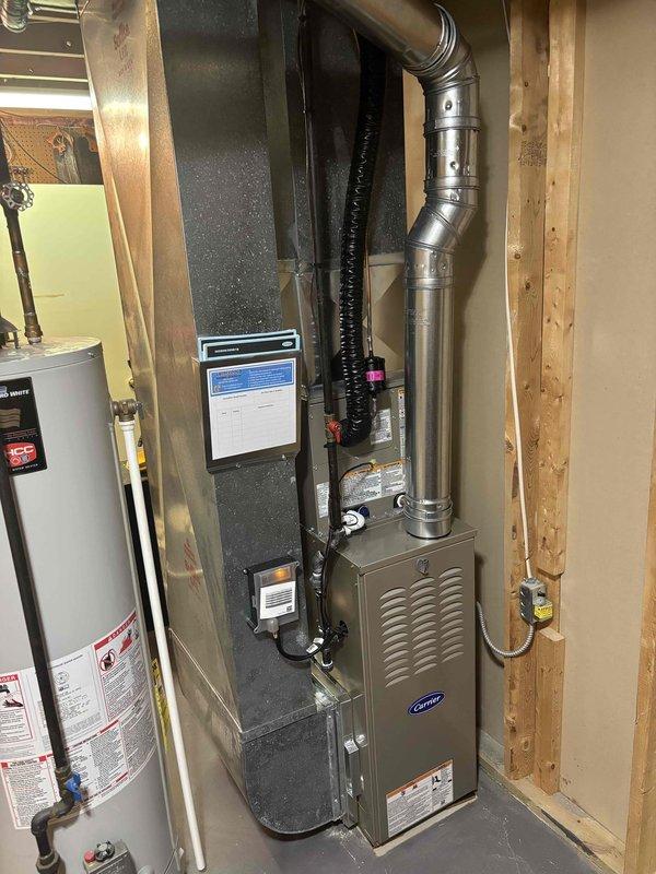 Completed full HVAC system installation in residential basement mechanical room. Installed new Carrier furnace unit with associated metallic ductwork, including rigid metal pipes and aluminum flexible ducting with proper vertical and horizontal connections. Installed black corrugated flexible condensate line and integrated system with existing Bradford White water heater plumbing. Routed all ductwork through unfinished basement space with proper support and connections to distribution system. Verified all mechanical connections, tested system operation, and confirmed proper airflow through installed ductwork. Installation includes complete furnace and air conditioning system with all necessary ventilation components and connections per specifications.