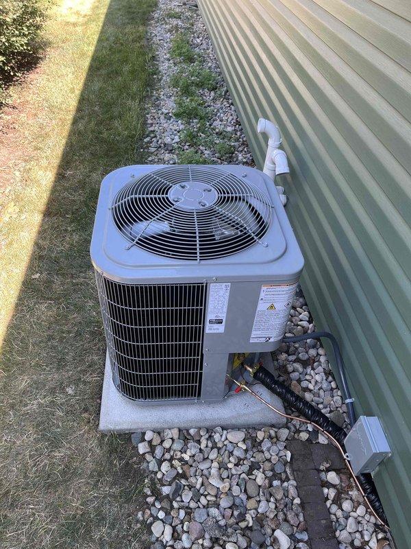Successfully completed full air conditioning system replacement at residential property. Removed existing outdoor condensing unit and installed new unit on concrete pad with proper leveling and stabilization. Connected refrigerant lines with appropriate insulation, installed condensate drain line with PVC piping routed along exterior wall, and mounted electrical disconnect box per code requirements. Unit positioned on existing concrete pad surrounded by river rock landscaping for proper drainage and airflow clearance. Verified all electrical connections, tested system operation, and confirmed proper refrigerant charge and airflow through condenser fan assembly. Installation meets manufacturer specifications and local building codes.