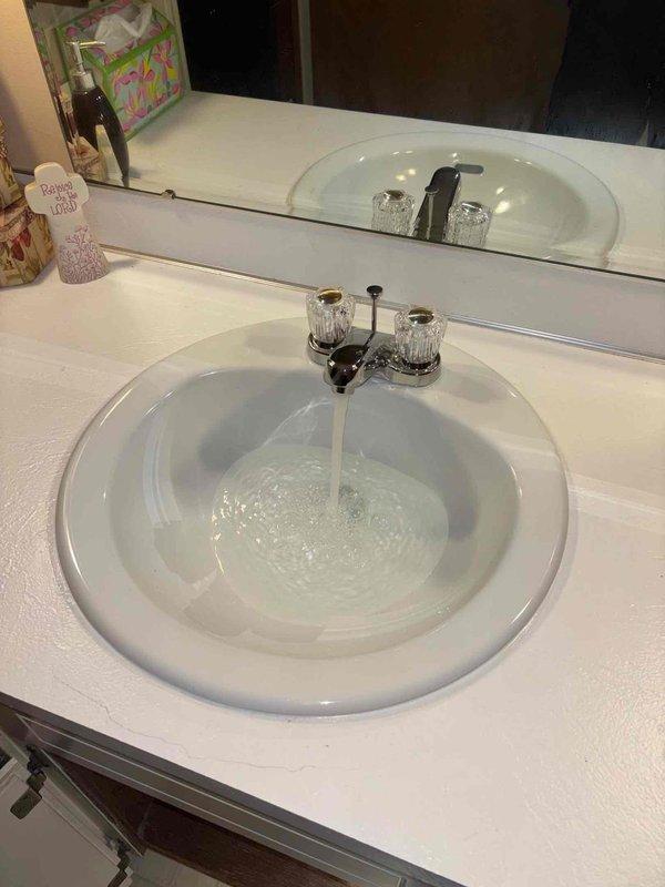 Completed bathroom sink faucet installation and drain assembly replacement. Installed new chrome two-handle faucet with clear acrylic handles, connected flexible braided supply lines, and replaced PVC P-trap drainage system with proper venting. Tested all connections for leaks and verified proper water flow and drainage operation.