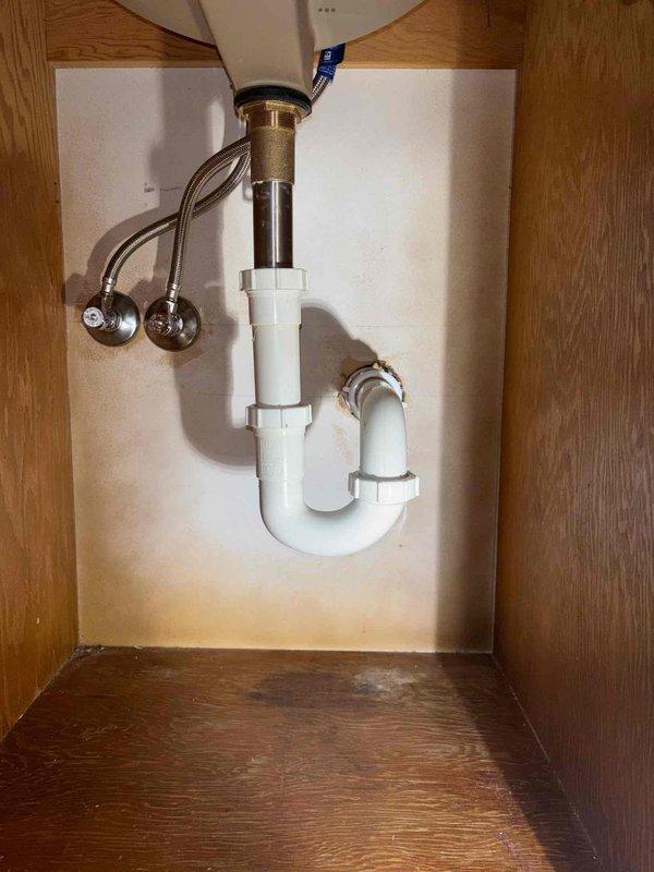 Completed bathroom sink faucet installation and drain assembly replacement. Installed new chrome two-handle faucet with clear acrylic handles, connected flexible braided supply lines, and replaced PVC P-trap drainage system with proper venting. Tested all connections for leaks and verified proper water flow and drainage operation.