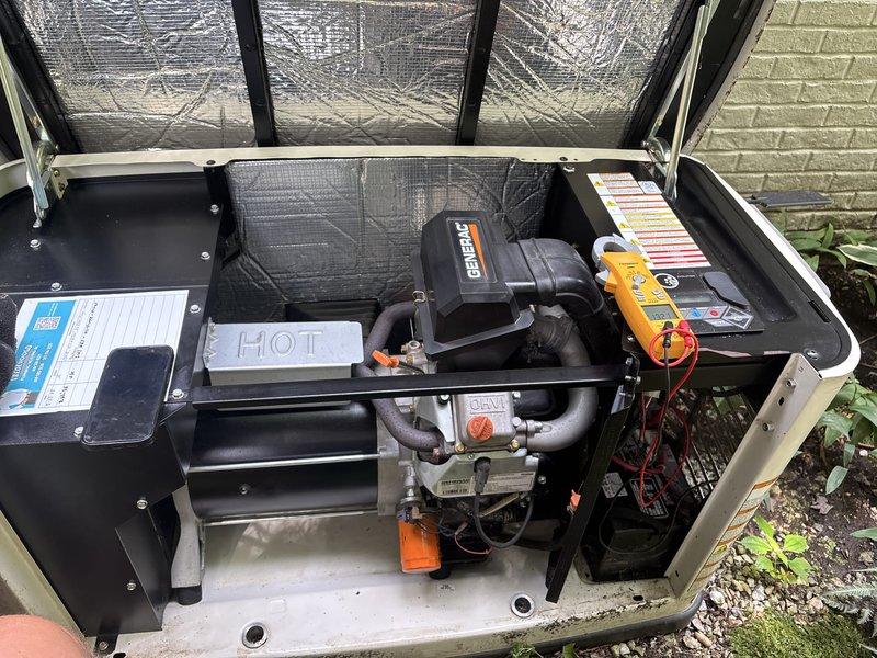 Responded to maintenance warning light on 11-year-old Generac generator that had been illuminated for several weeks following notification during previous AC service visit. Performed diagnostic inspection and testing of generator system using multimeter to assess electrical components and operational status. Inspected internal components including heat exchanger, control panel, and wiring connections. Evaluated unit condition, noting vegetation encroachment and moss accumulation on concrete pad surrounding equipment. Documented system status with photographs for service records. Generator system confirmed as registered and under contract for ongoing maintenance support.