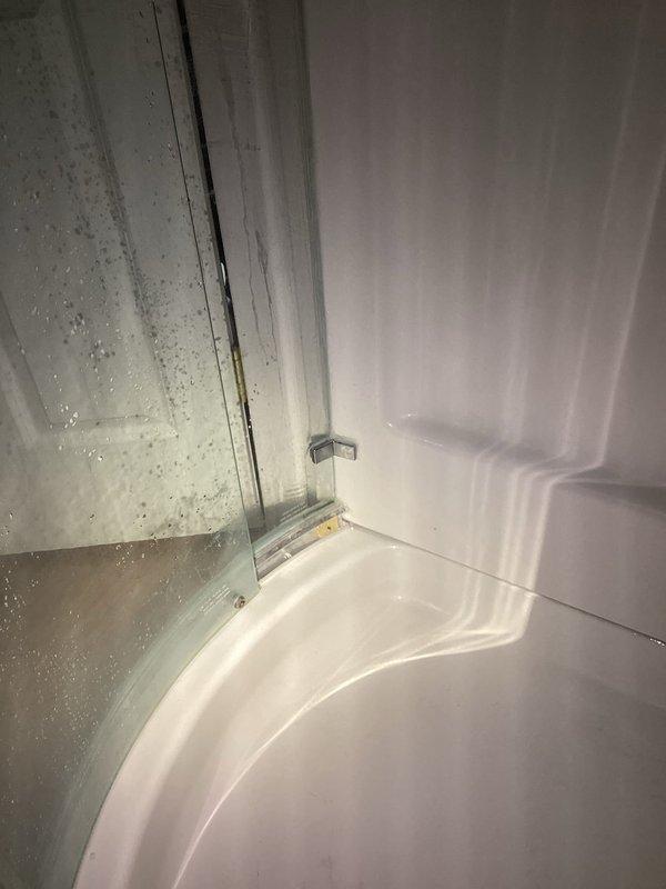 Responded to follow-up service call for persistent water leak originating from shower enclosure that was not resolved by previous repair attempt. Upon inspection, observed active moisture and water droplets on glass shower door and surrounding surfaces, with visible water staining on baseboard and wall areas indicating ongoing leak penetrating through flooring into garage space below. Documented conditions with photographs showing condensation patterns and water accumulation points to identify leak source and assess extent of water intrusion damage for proper remediation.