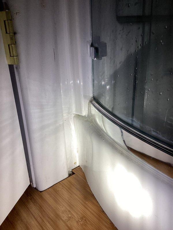Responded to follow-up service call for persistent water leak originating from shower enclosure that was not resolved by previous repair attempt. Upon inspection, observed active moisture and water droplets on glass shower door and surrounding surfaces, with visible water staining on baseboard and wall areas indicating ongoing leak penetrating through flooring into garage space below. Documented conditions with photographs showing condensation patterns and water accumulation points to identify leak source and assess extent of water intrusion damage for proper remediation.